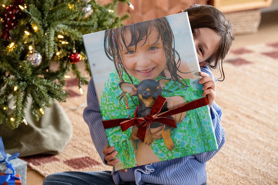 Lita jente under juletreet som holder en stor fotobok med et fløyelsbånd rundt og et bilde av seg selv med en chihuahua på forsiden, som illustrerer fotoknudsen sin sjekkliste med julegavetips for en personlig fotogave.