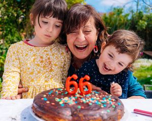 Bestemor med to barnebarn som lykkelig blåser ut bursdagslys.