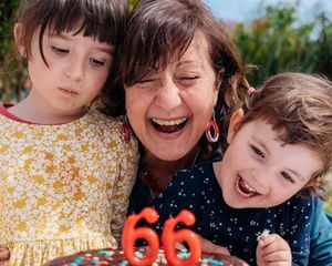 En bestemor feirer 66-årsdagen sin med sine to barnebarn ved siden av seg og skal til å blåse ut lysene på kaken, som inspirasjon til bursdagsgaver fra fotoknudsen sin ultimate bursdagsgaveguide.