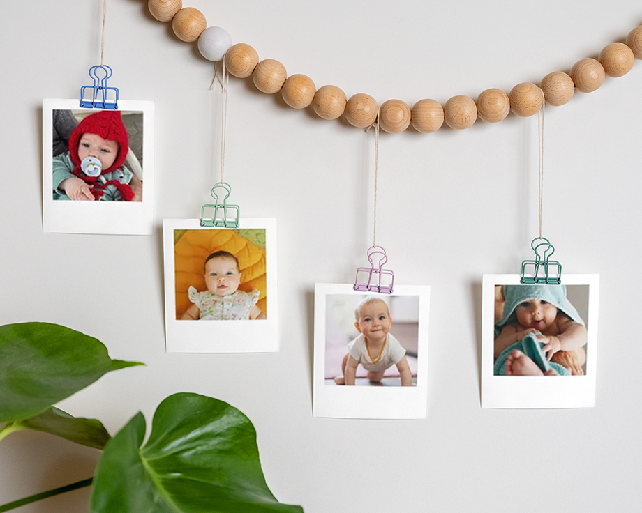 Babybilder klistret på en treperlekrans som henger på en vegg.