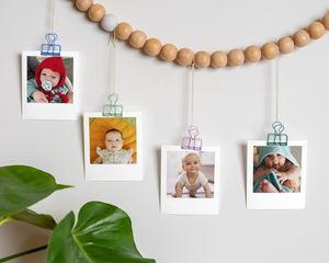 Babybilder klistret på en treperlekrans som henger på en vegg.