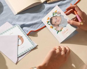Hånd som skriver et personlig babyfotokort på et skrivebord.