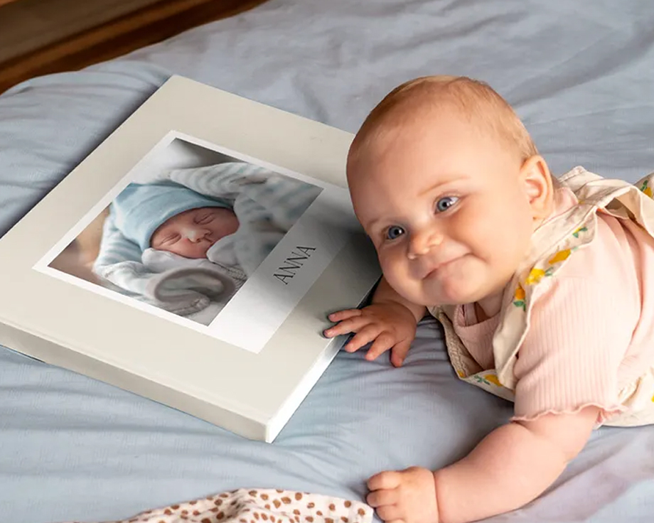 Baby som ligger ved siden av en personlig fotobok med et babybilde på omslaget.