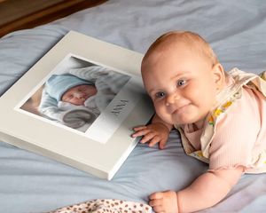 Baby som ligger ved siden av en personlig fotobok med et babybilde på omslaget.